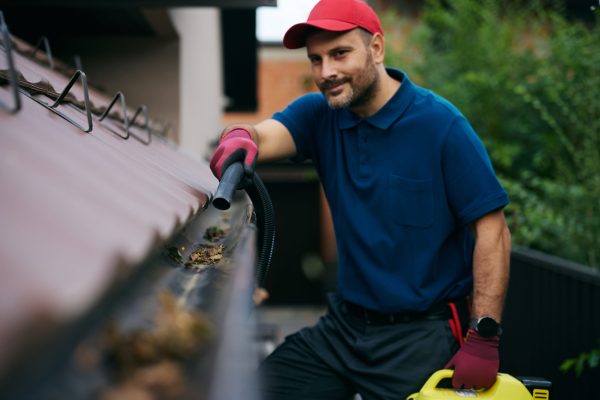 Close up of maintenance worker cleaning gutters on roof with a blower. Copy space.